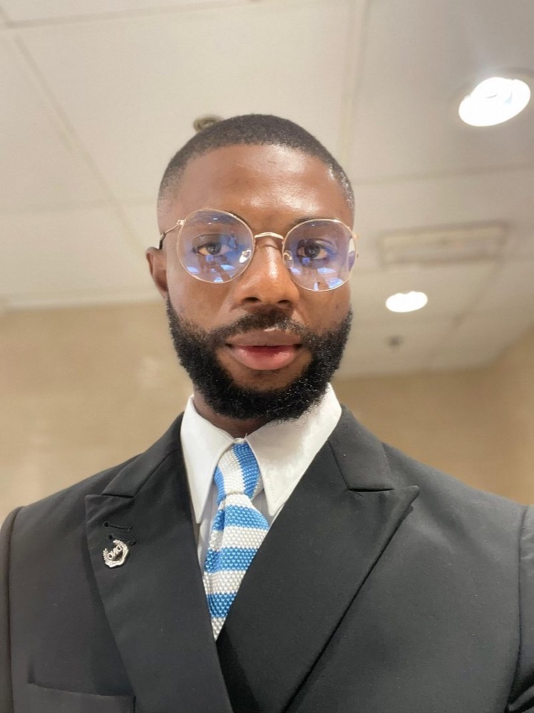 Clinton Nkweke in a black suit and striped tie